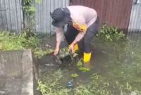 Salah satu Personil Ditsamapta Poldasu sedang mengeluarkan batu padas yang sebabkan saluran tumpat sehingga air menggenangi jalan. 