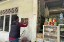 Salah satu Personel Polres Simalungun melakukan penempelan stiker di dinding Kios warga.