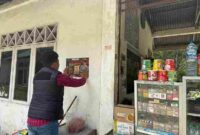 Salah satu Personel Polres Simalungun melakukan penempelan stiker di dinding Kios warga.
