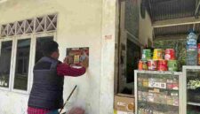 Salah satu Personel Polres Simalungun melakukan penempelan stiker di dinding Kios warga.