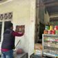 Salah satu Personel Polres Simalungun melakukan penempelan stiker di dinding Kios warga.