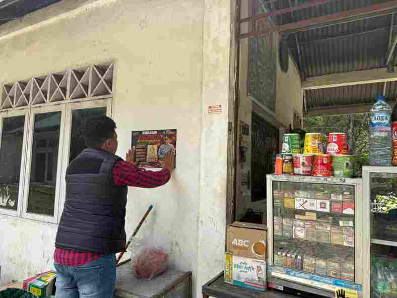 Salah satu Personel Polres Simalungun melakukan penempelan stiker di dinding Kios warga.